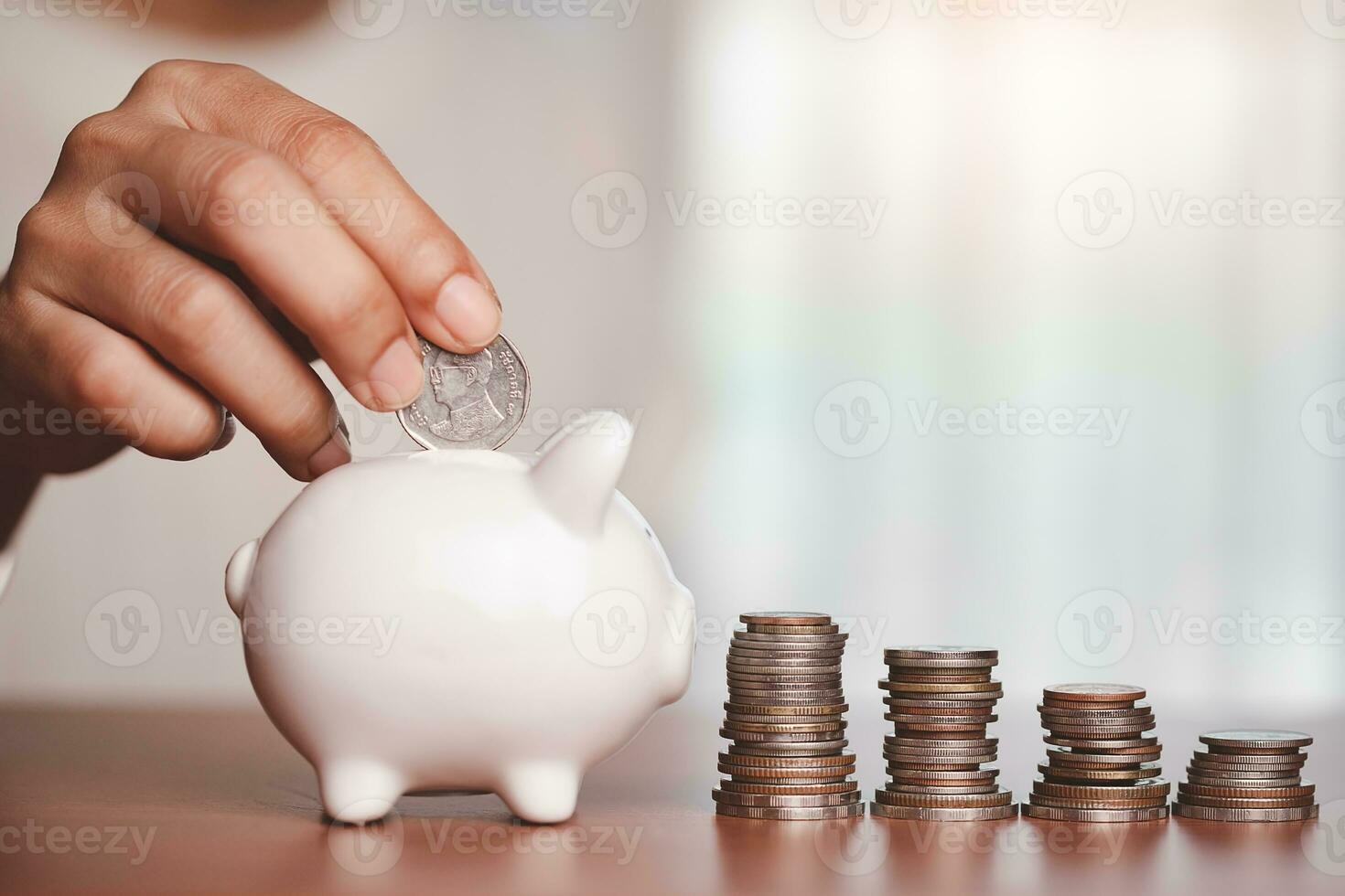 Hand saving a coin into piggy bank with step of coins and money on the wooden table photo