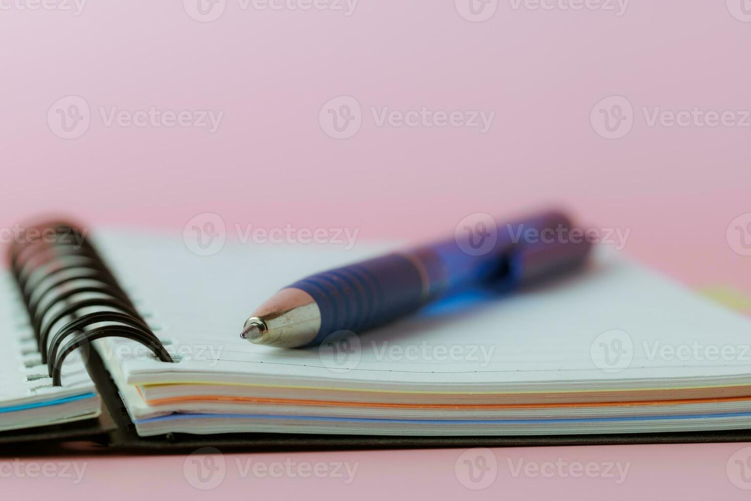Selective focus of a pen on a notebook against pink background photo