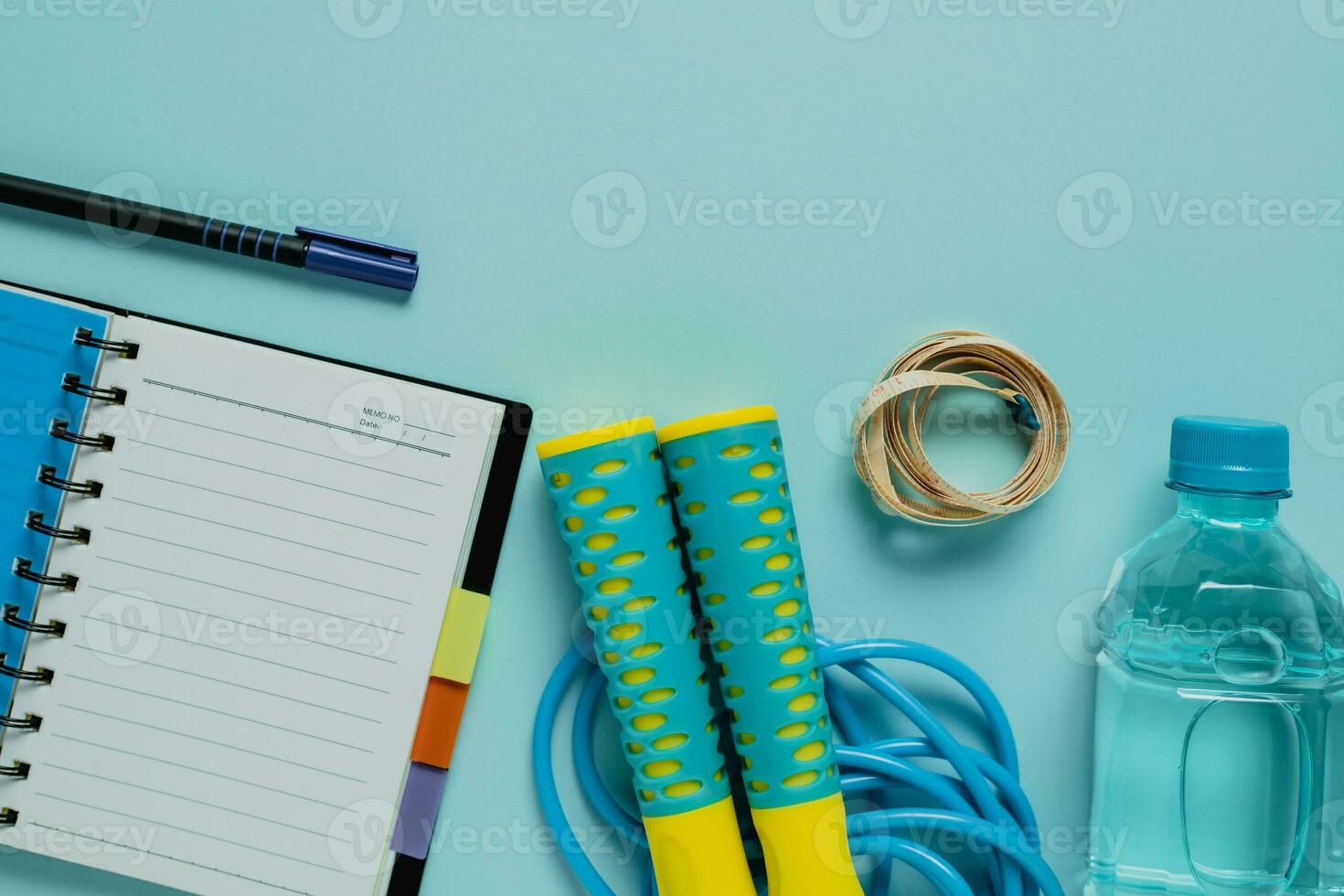 Notebooks with measure tape, fresh drinking water, jump rope on blue background photo