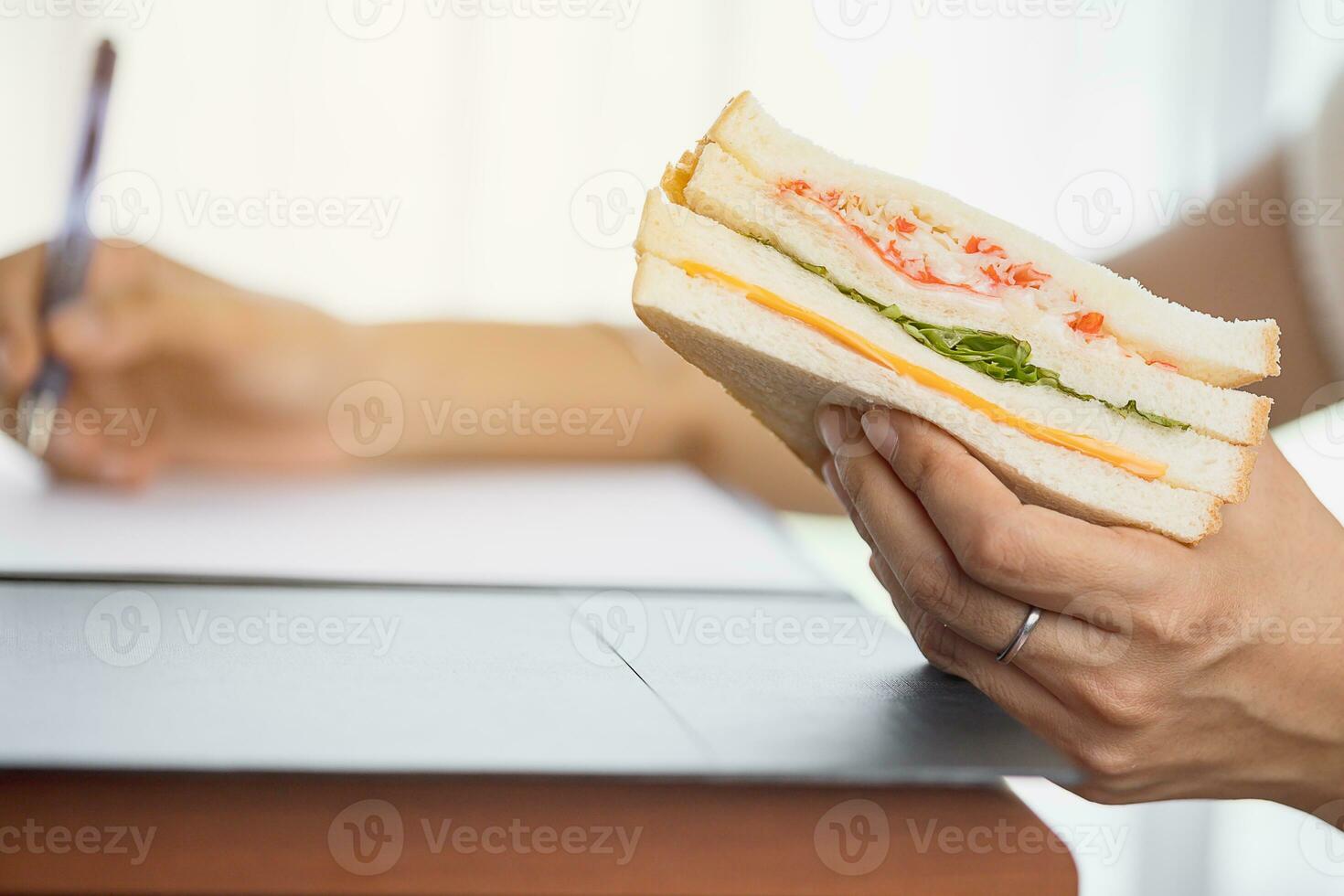 Hand holding a delicious sandwich while doing work photo