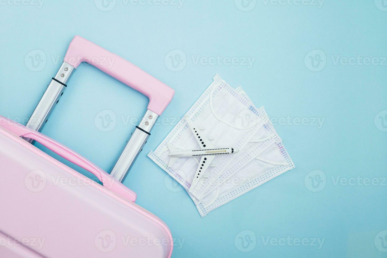 Pink luggage with white airplane model and hygiene face mask on blue background photo