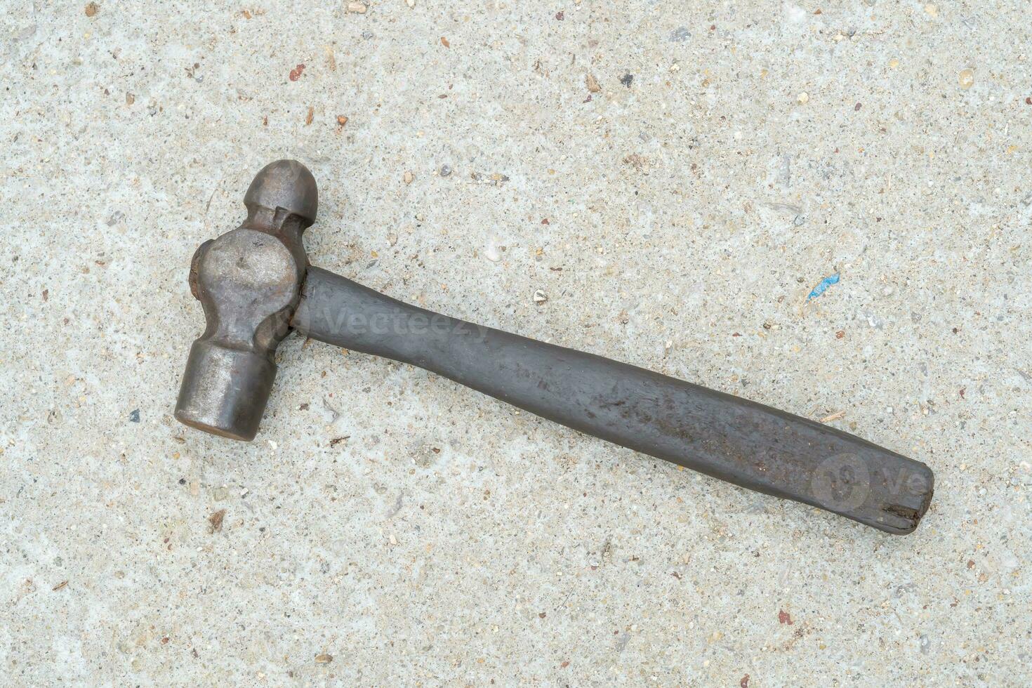 Single dirty old metal or iron hammer with wooden handle laying down on concrete floor. Flat lay photo