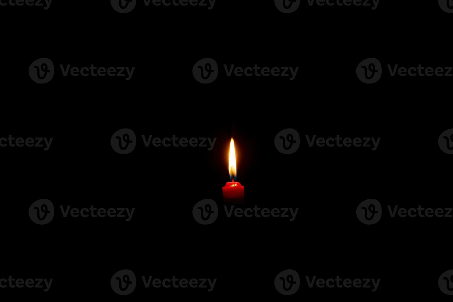 Single burning candle flame or light glowing on a small red candle on black or dark background on table in church for Christmas, funeral or memorial service with copy space. photo