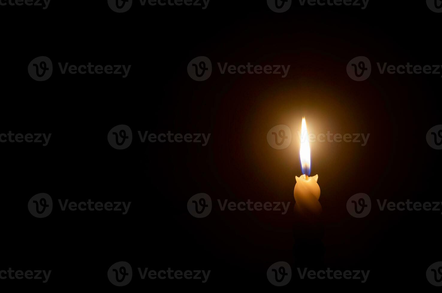 A single burning candle flame or light glowing on a white spiral candle on black or dark background on table in church for Christmas, funeral or memorial service with copy space. photo