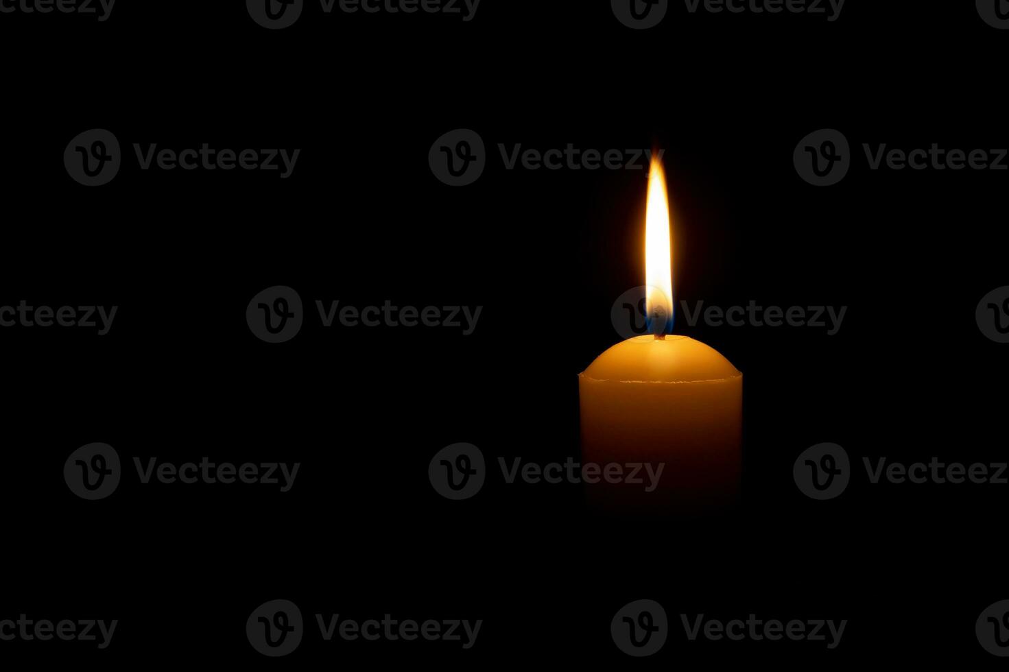 Single burning candle flame or light glowing on a big yellow candle on black or dark background on table in church for Christmas, funeral or memorial service with copy space. photo