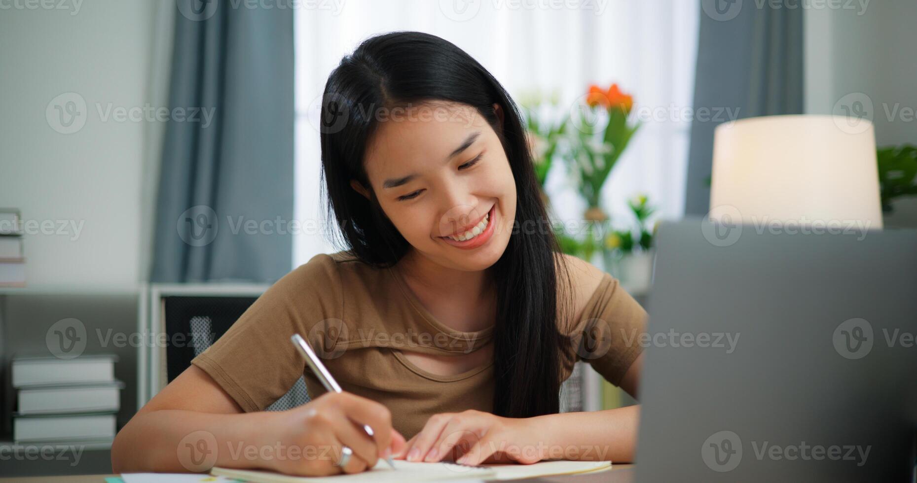 oung Asian woman working with a laptop and writing on paper on a desk photo