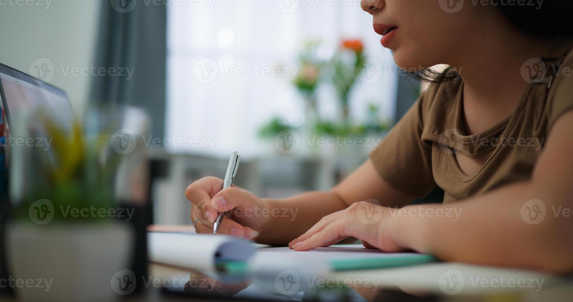 oung Asian woman working with a laptop and writing on paper on a desk photo