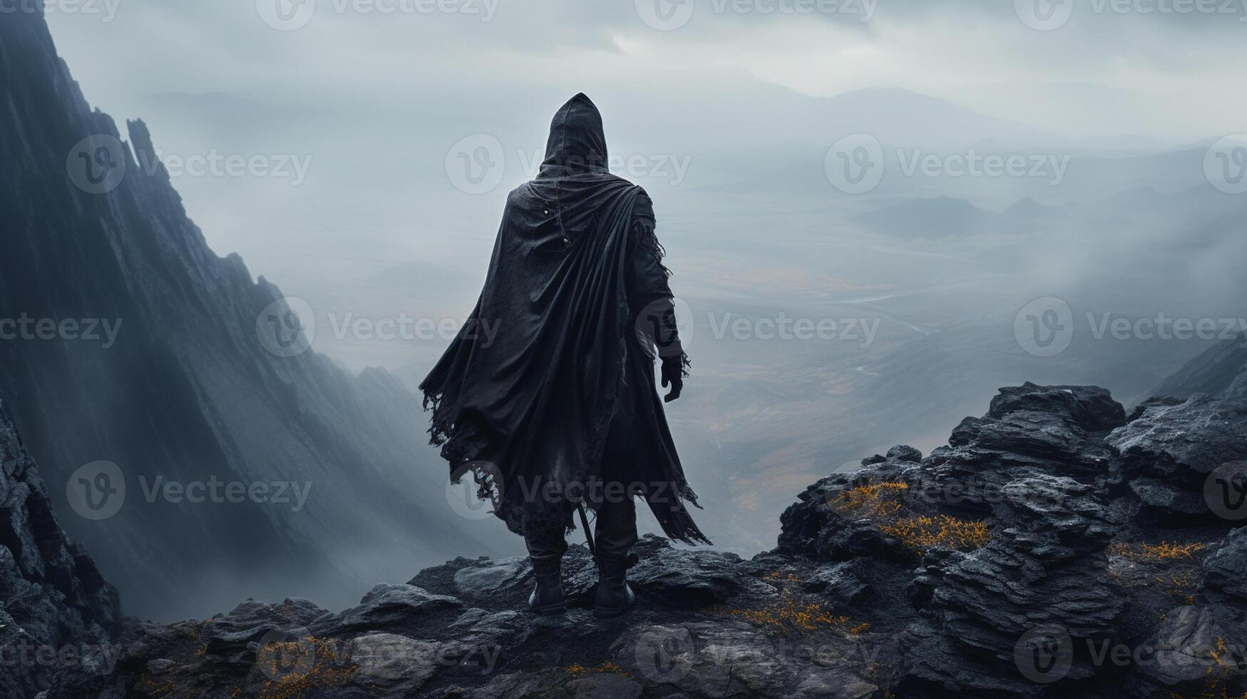A hooded warrior man stands atop a rugged mountain peak photo