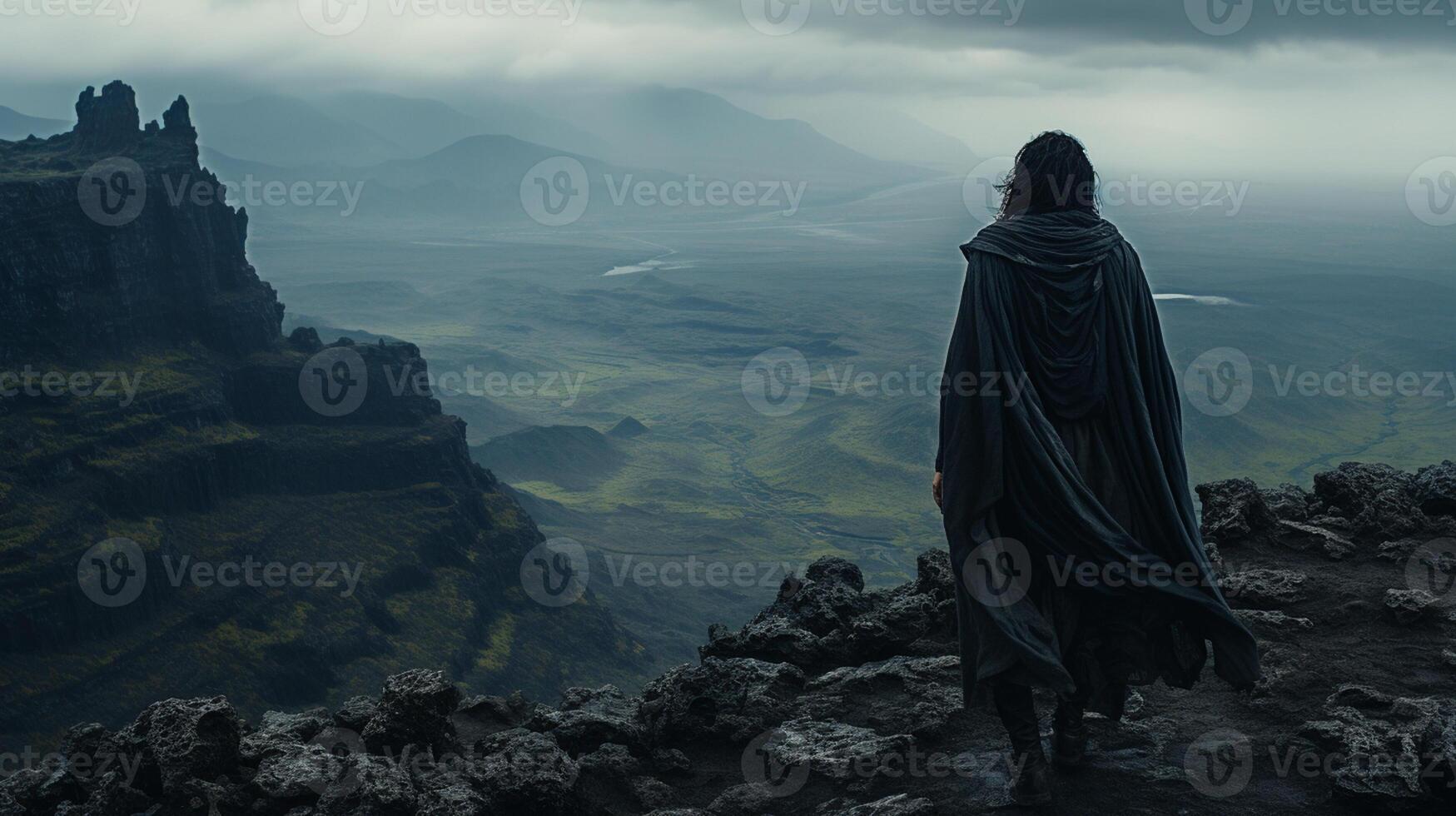 A hooded warrior man stands atop a rugged mountain peak photo