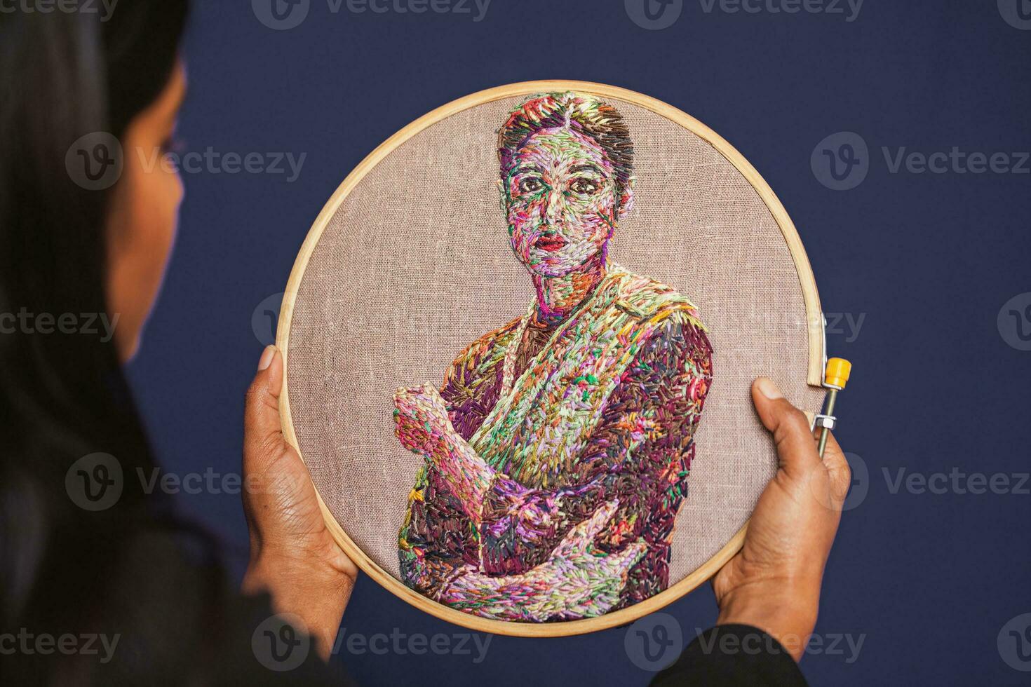 a woman holding up a embroidered portrait of a woman photo
