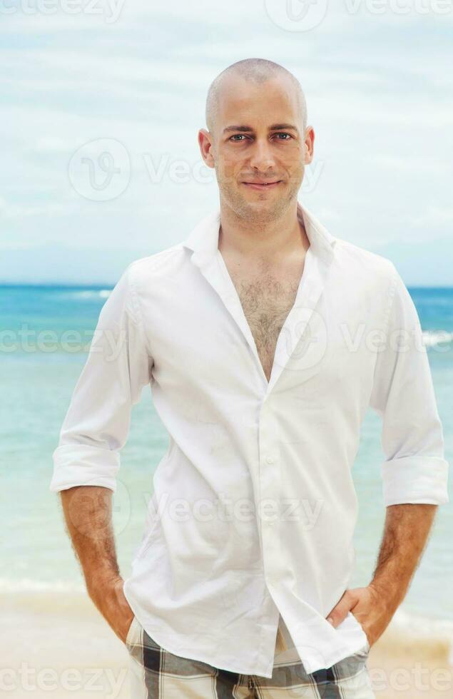 a bald man in a white shirt standing on the beach photo