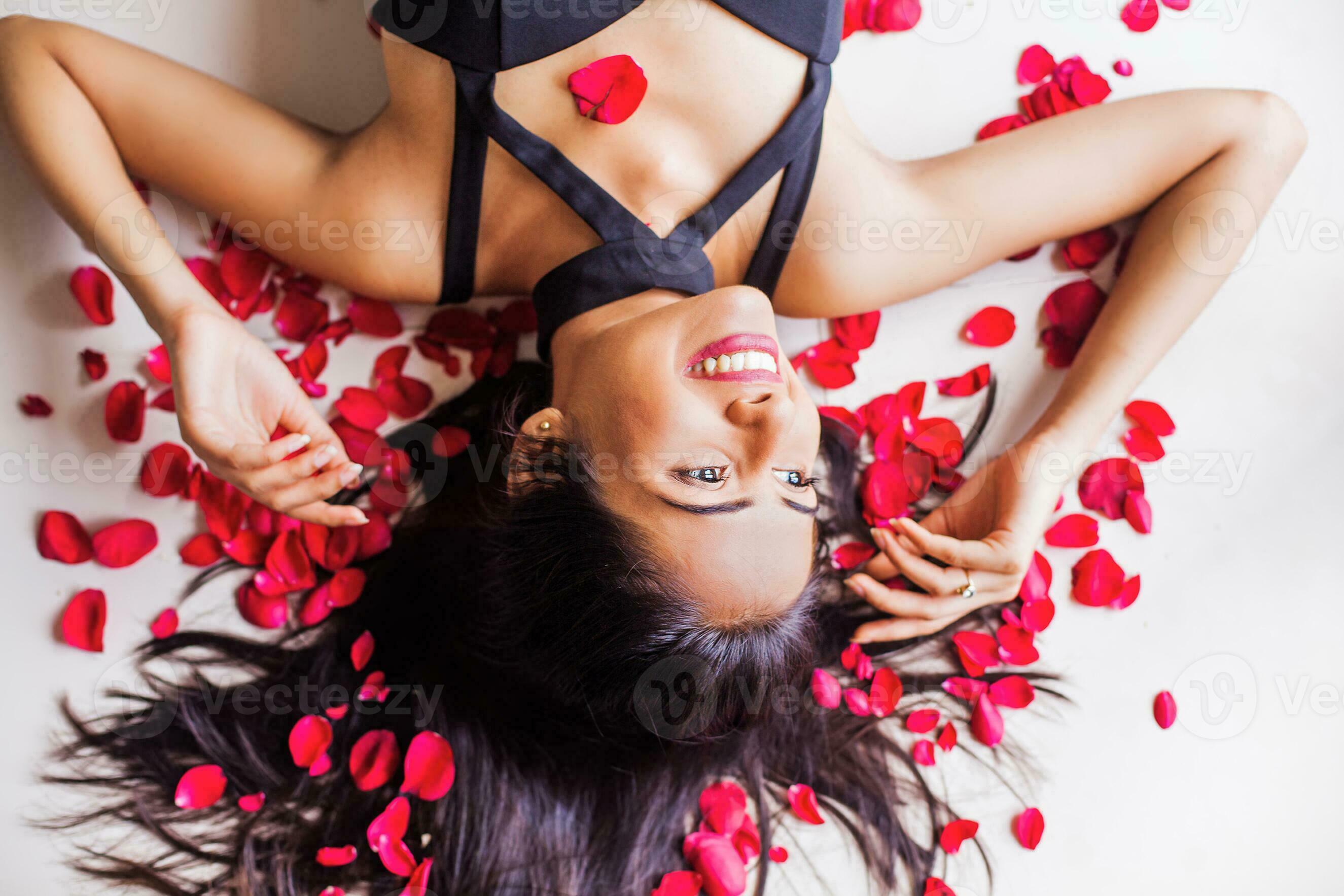 A beautiful smiling Indian woman with her untied hair wearing dress lying  on a bed scattered with red rose petals 26415658 Stock Photo at Vecteezy
