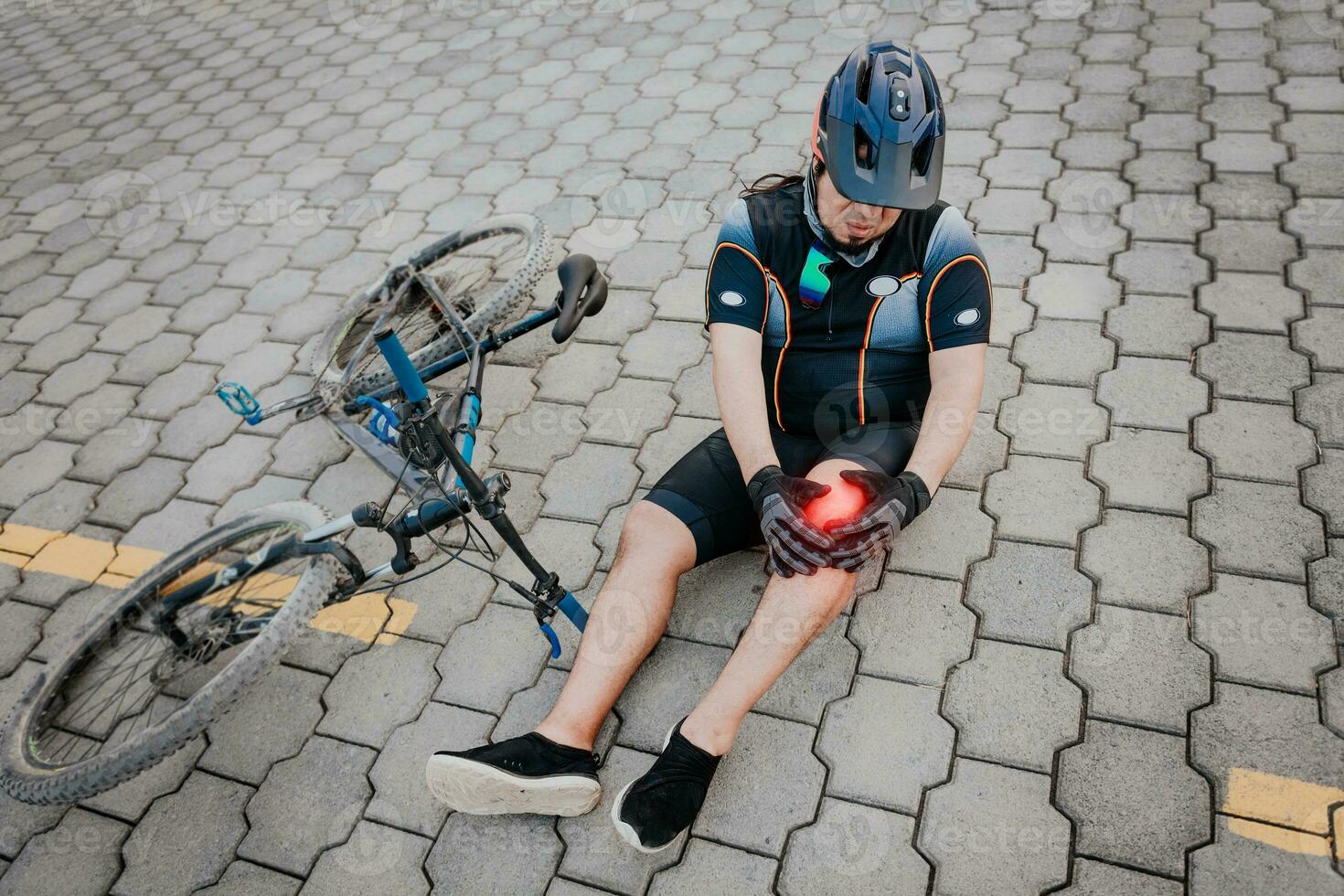 Unhappy cyclist sitting on the pavement with knee pain. Concept of a cyclist with knee injury outdoors, Cyclist with knee pain outdoors photo