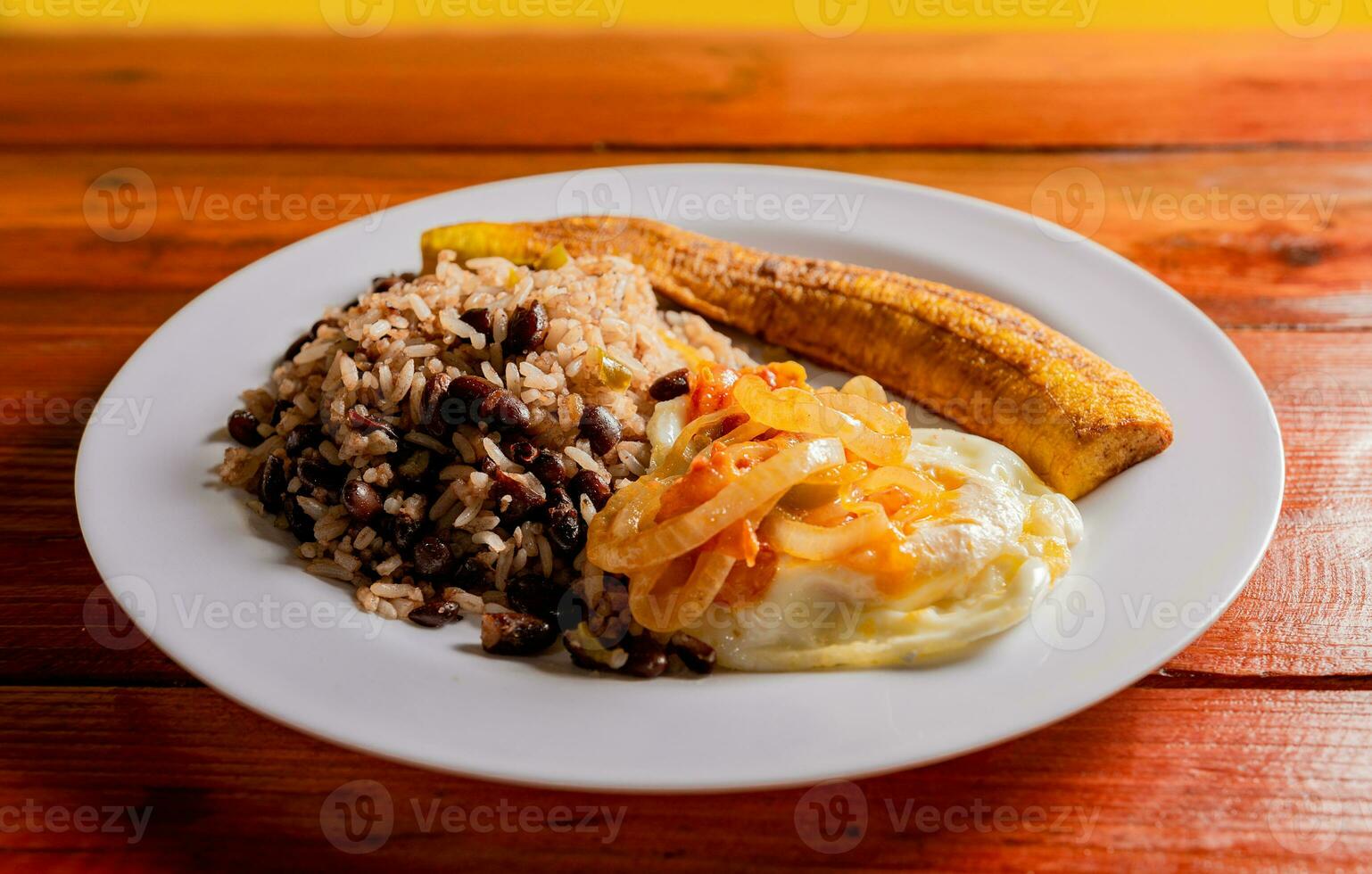 Gallopinto dish with ripe and fried eggs served on wooden table. Gallopinto breakfast with fried eggs and maduro on the table. Concept of typical foods of Latin America photo