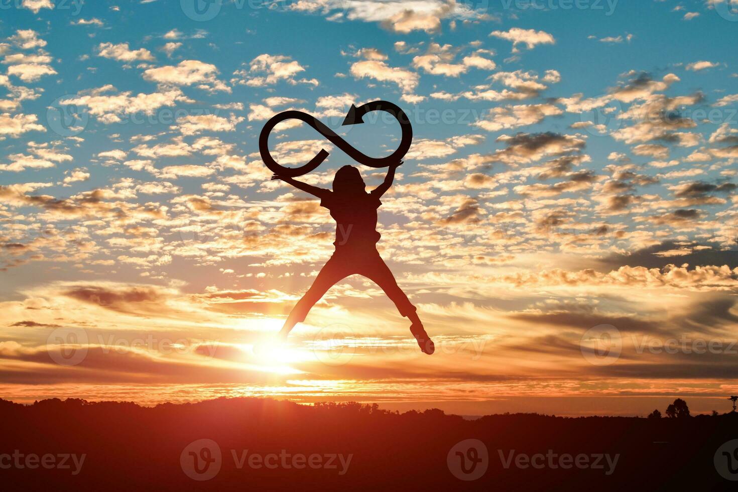 Silhouette of woman jumping and holds an infinity symbol at sunset background. photo