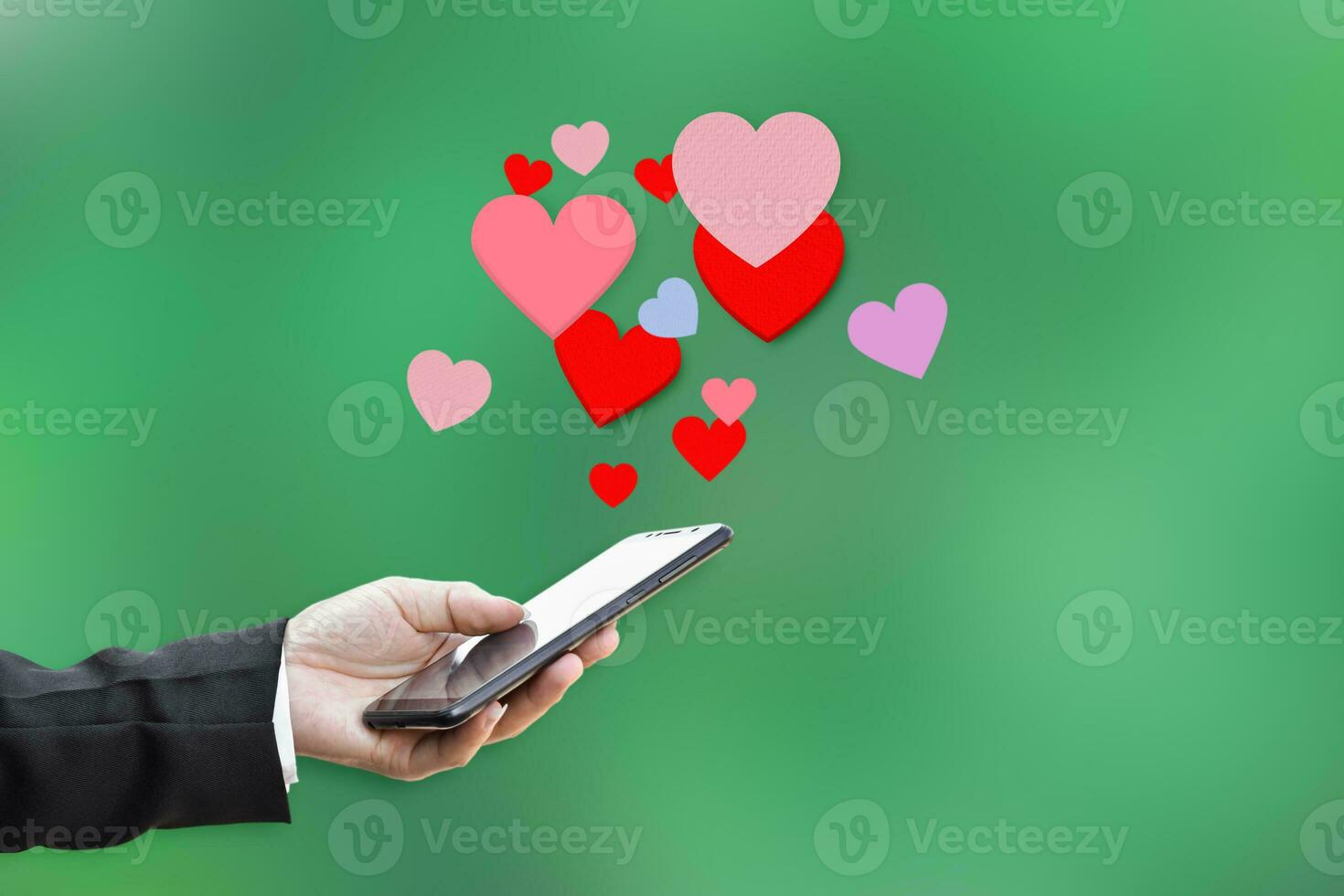 Male hands holding mobile phone with hearts, Love symbol on green background. Valentine's day concept. photo