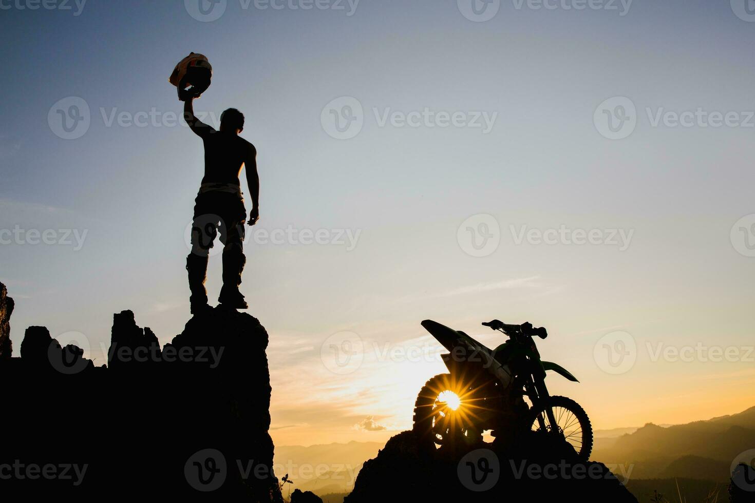 Man with motocross bike against beautiful lights, silhouette of a man with  motocross motorcycle On top of rock high mountain at beautiful sunset, enduro motorcycle travel concept. photo