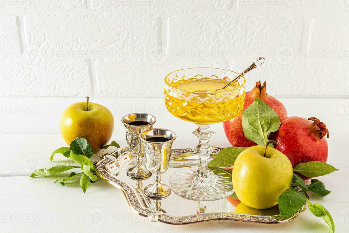 Beautiful still life with ripe pomegranates and apples, a silver glass of wine and a bowl of honey. White background. The concept of Rosh Hashanah. photo