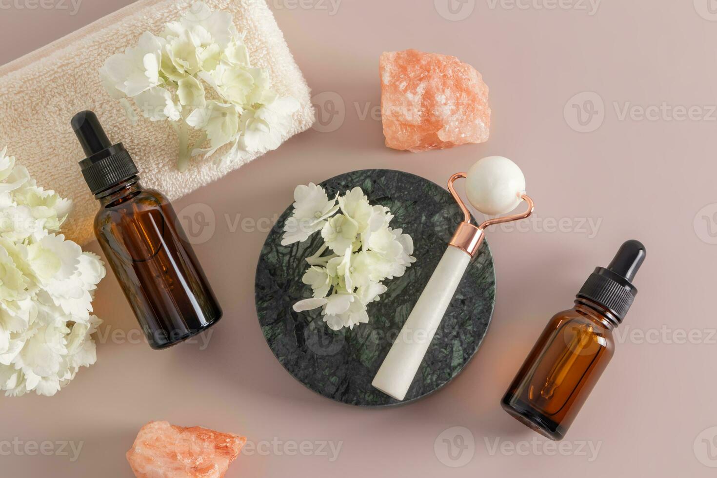 A set of cosmetics in glass bottles with a pipette and a white stone roller on a round marble podium. home self-care. top view. photo