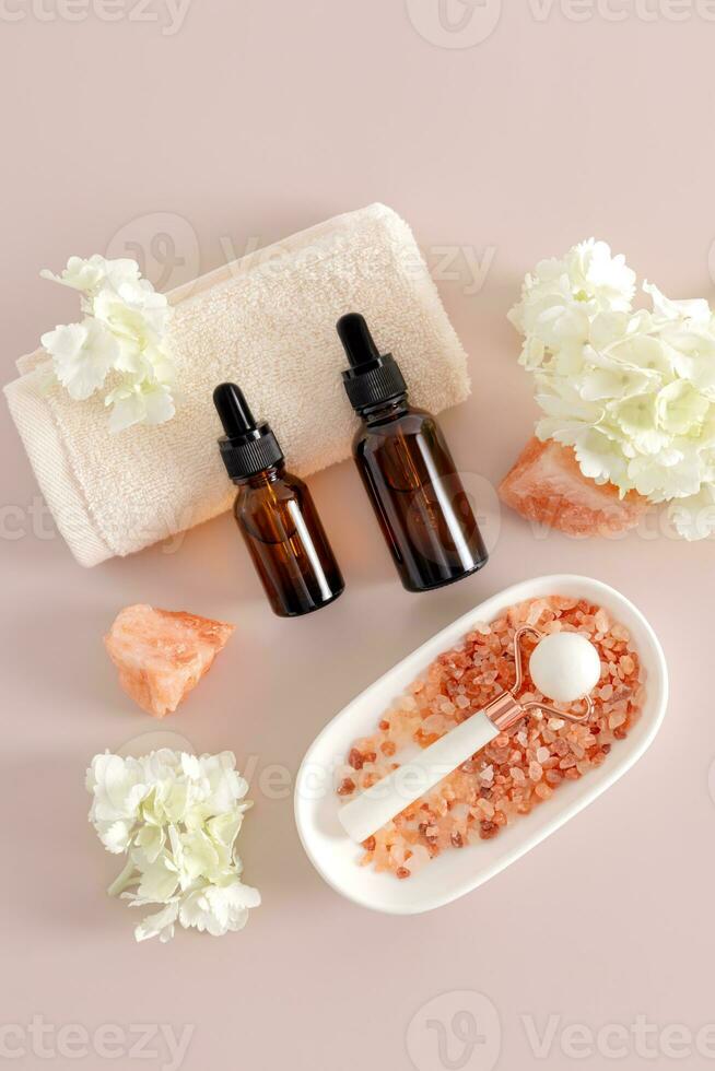 A set of cosmetics in bottles with a pipette, a white roller and bath salts on a pastel background. The concept of self-care. spa. Top vertical view. photo