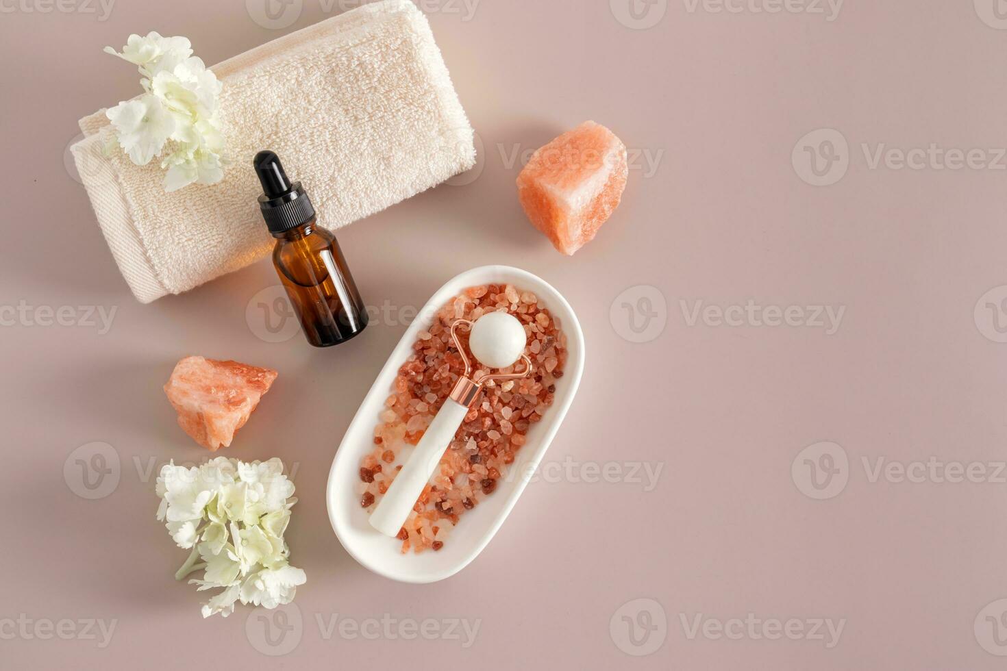 A bottle of cosmetic product on the roller of the towel , white stone massager in an oval bowl with bath salts. Top view . A copy space. photo