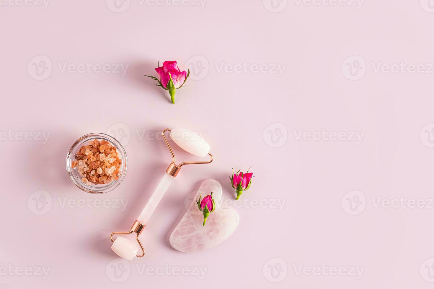 Rose quartz massager, gua sha scraper, salt in a bowl and small rosebuds. Top view. Pink background. A copy space. natural care. photo
