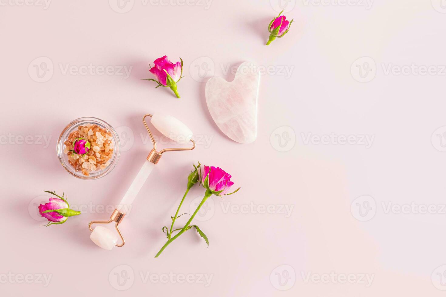 Roller massager for face, neck and decalte area Gua sha scraper on a pink background with small rosebuds. A copy of the space. The concept of beauty. photo