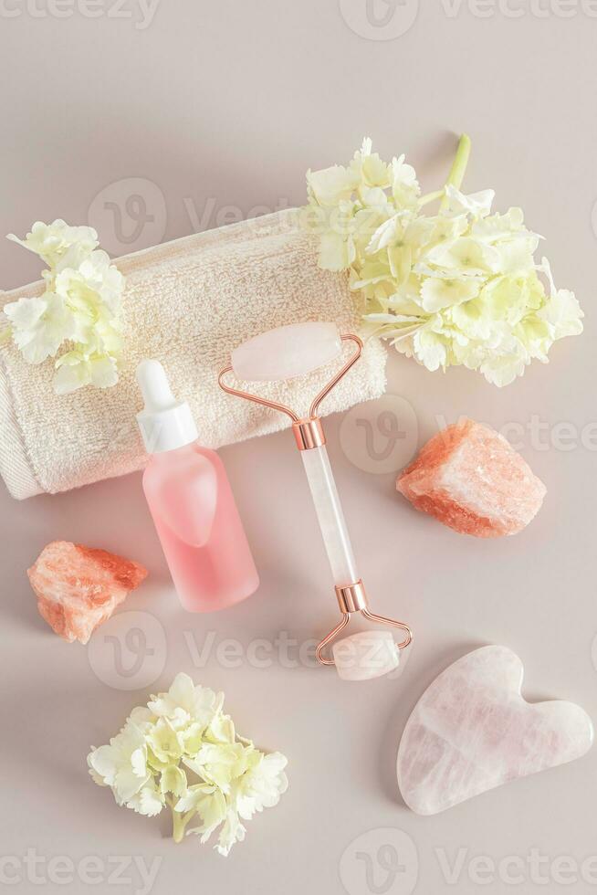 quartz roller massager, gua sha, matte bottle with a cosmetic product for maasage and face and body skin care. Vertical view. hydrangea flowers. photo