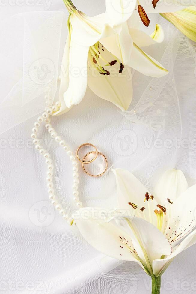 Chic vertical wedding background for design, layout, postcard, invitation. two gold wedding rings, a string of pearls and white lilies. photo