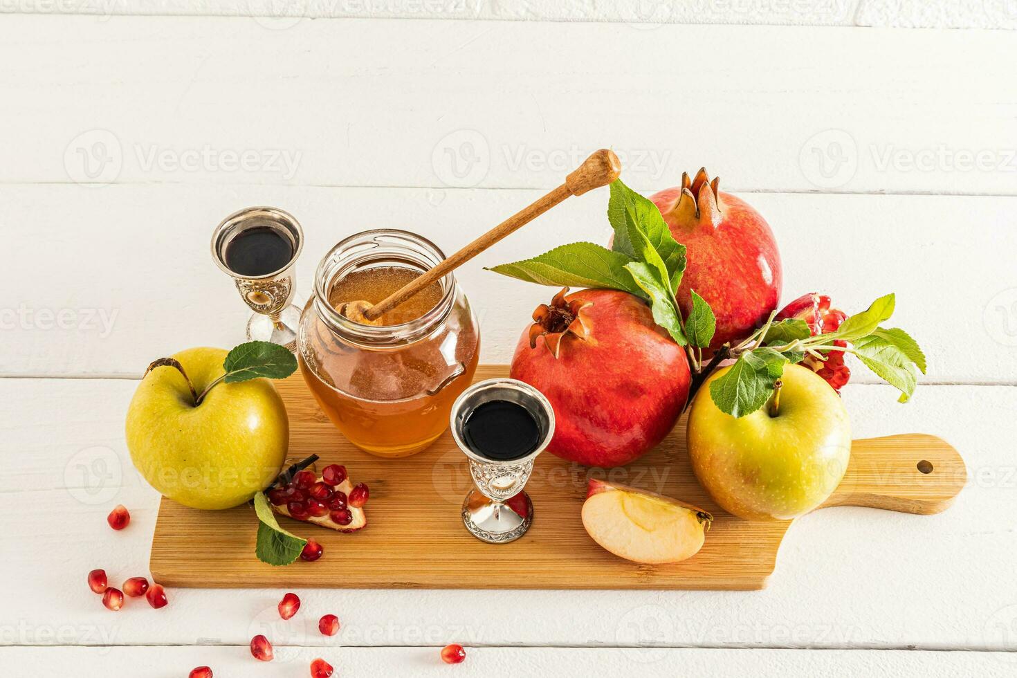 Beautiful still life with ripe pomegranates and apples, a glass silver of wine and a bowl of honey. White background. The concept of Rosh Hashanah. photo