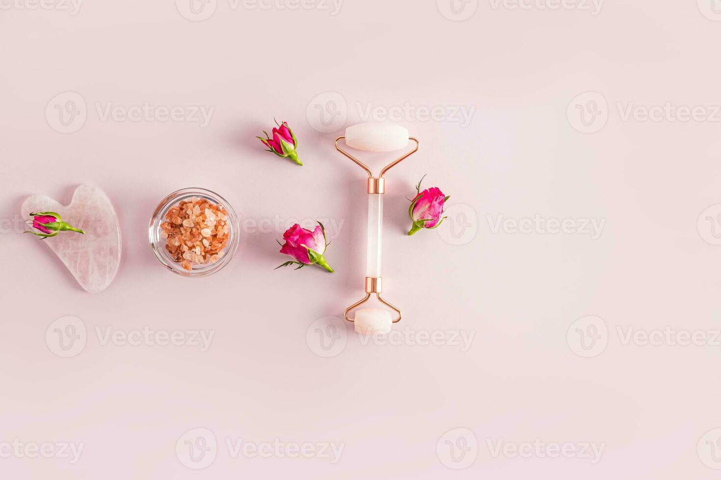 Rose quartz massager, gua sha scraper, salt in a bowl and small rosebuds. Top view. Pink background. A copy space. natural care photo