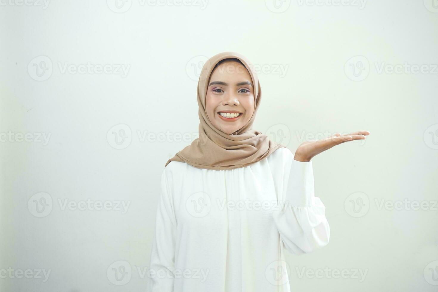 Smiling young Asian muslim woman in wearing casual clothes showing copy space on palm on white background photo