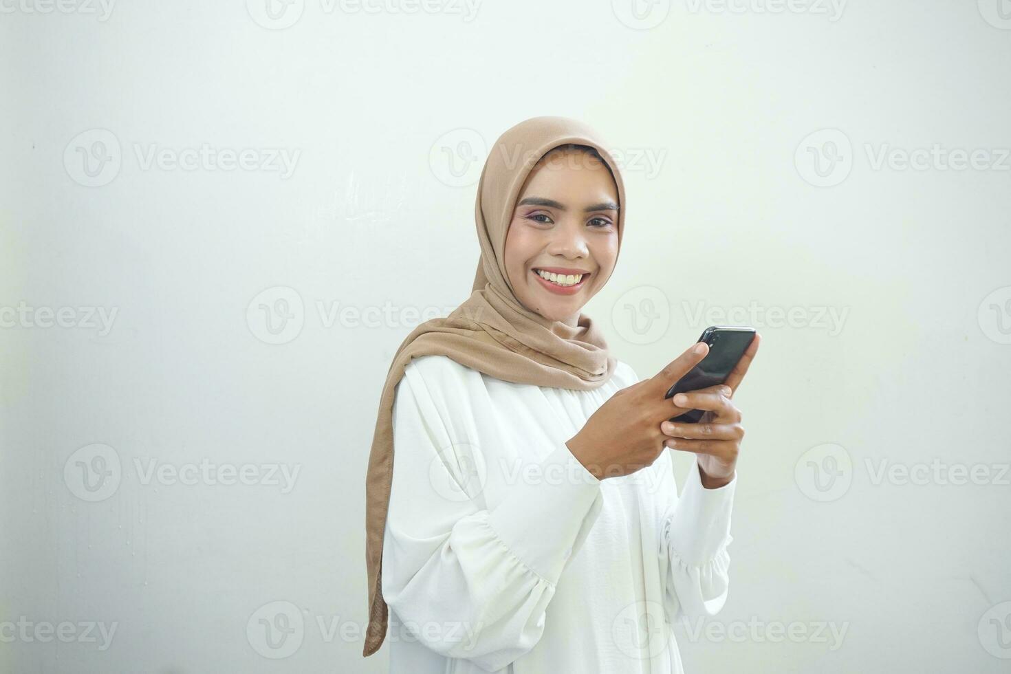 Beautiful smiling Asian Muslim woman wearing hijab Using mobile phone, typing sms message isolated on white background studio portrait. People religious lifestyle concept photo