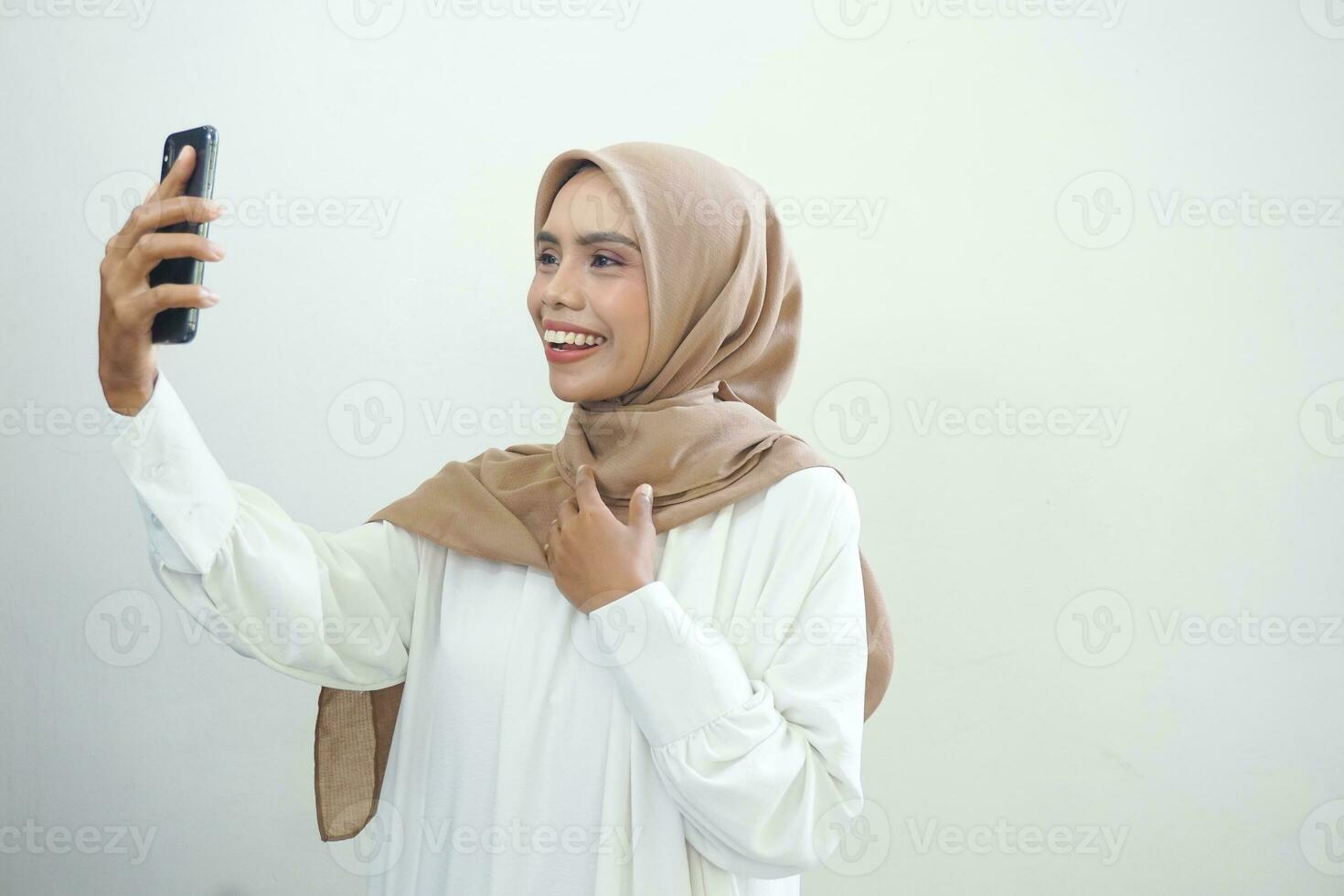 Excited beautiful Asian muslim woman showing mobile phone isolated over white background photo