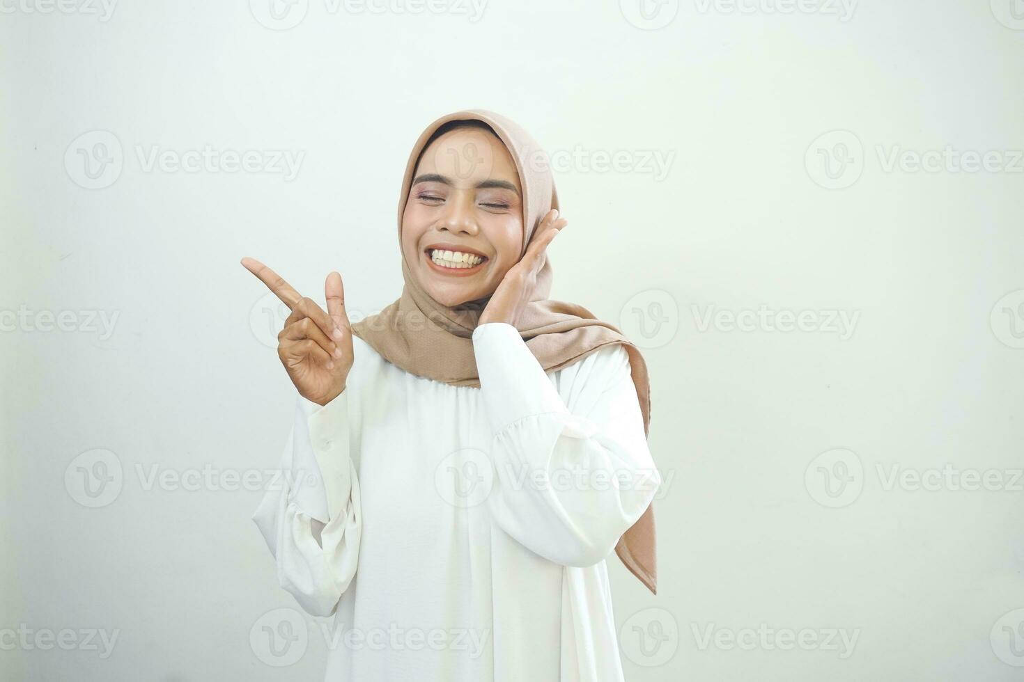 Cheerful beautiful Asian woman in white dress pointing fingers aside at copy space isolated over white background photo