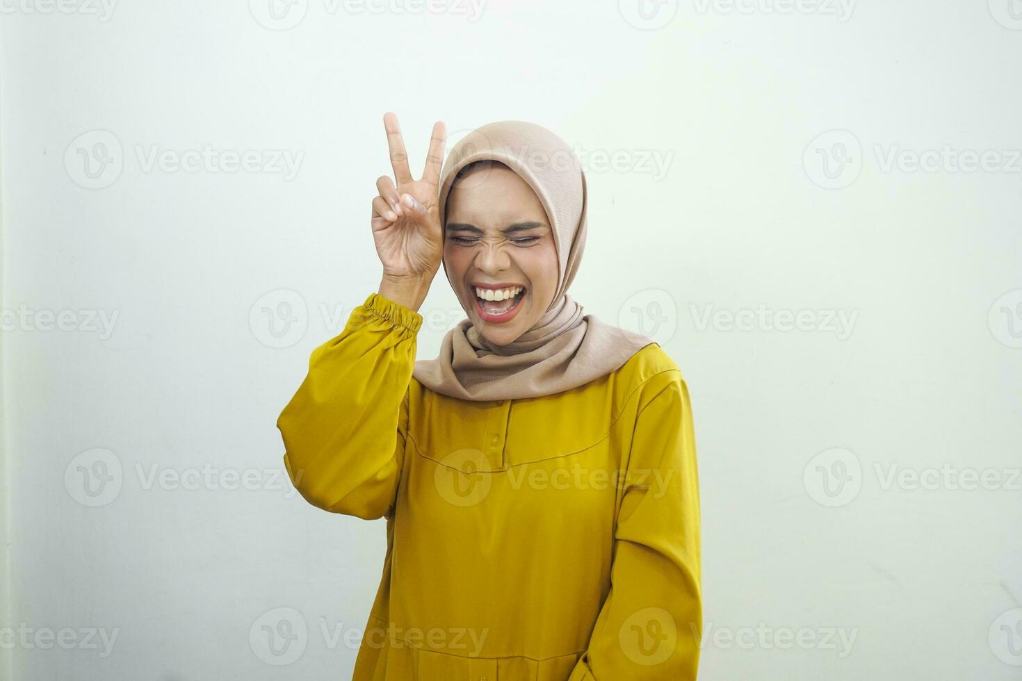Cheerful muslim girl in hijab showing peace gesture and posing to camera studio background with free space photo
