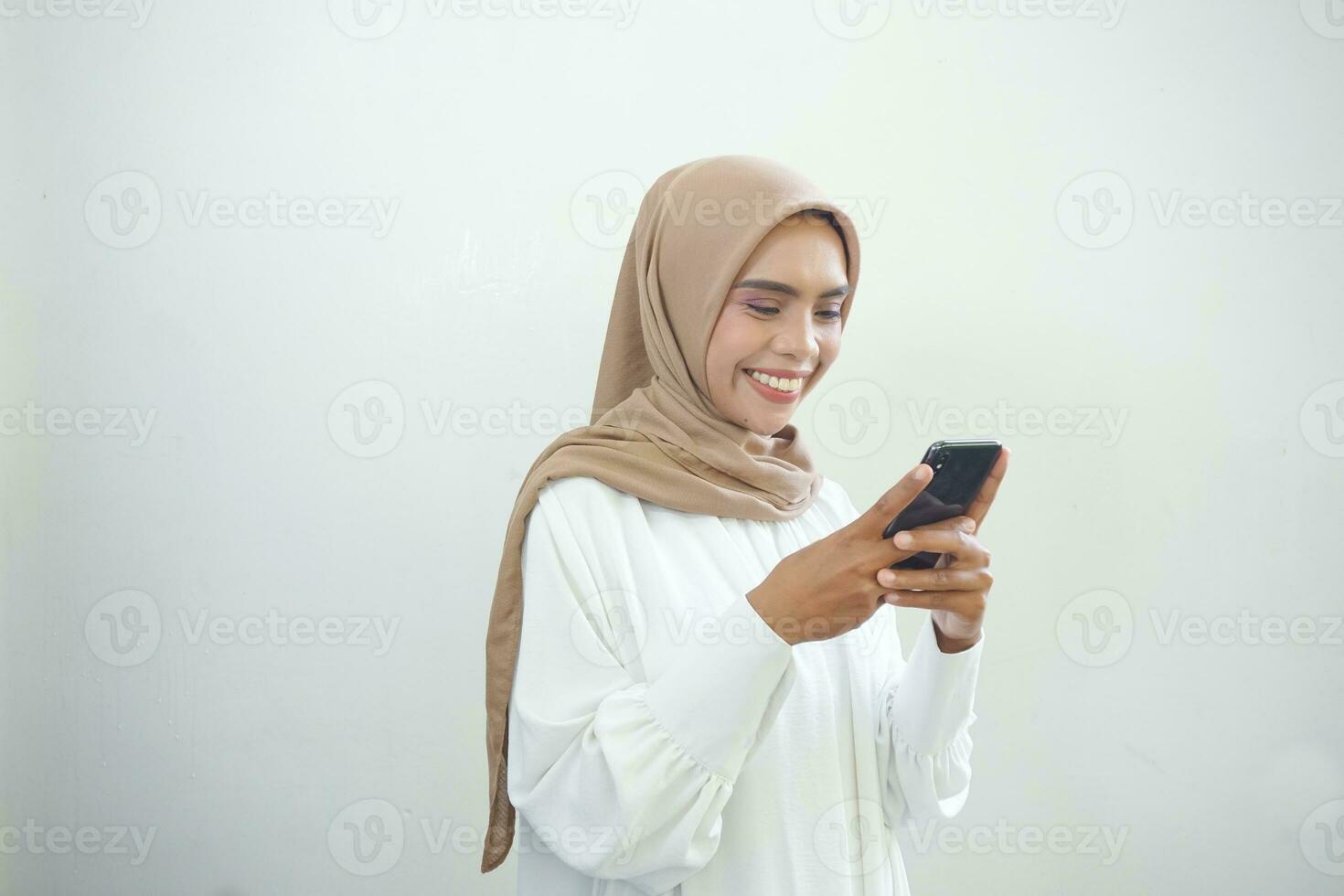 Beautiful smiling Asian Muslim woman wearing hijab holding mobile phone in hand isolated on white background studio portrait. People religious lifestyle concept photo