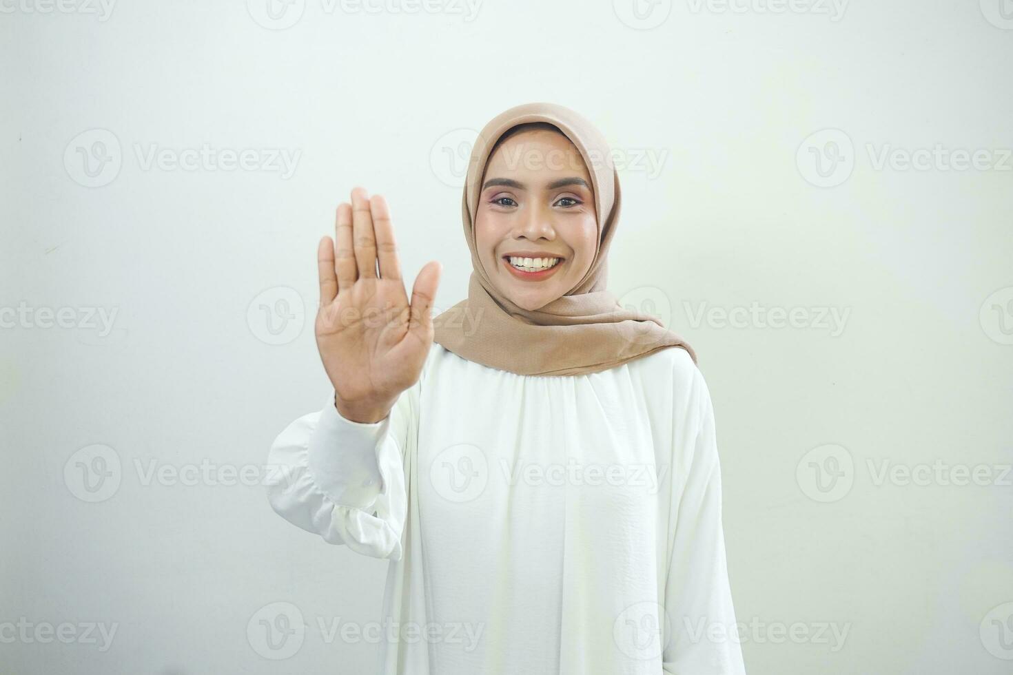 Serious young Asian Muslim woman dressed in casual white standing with outstretched hand showing stop gesture isolated over white background photo