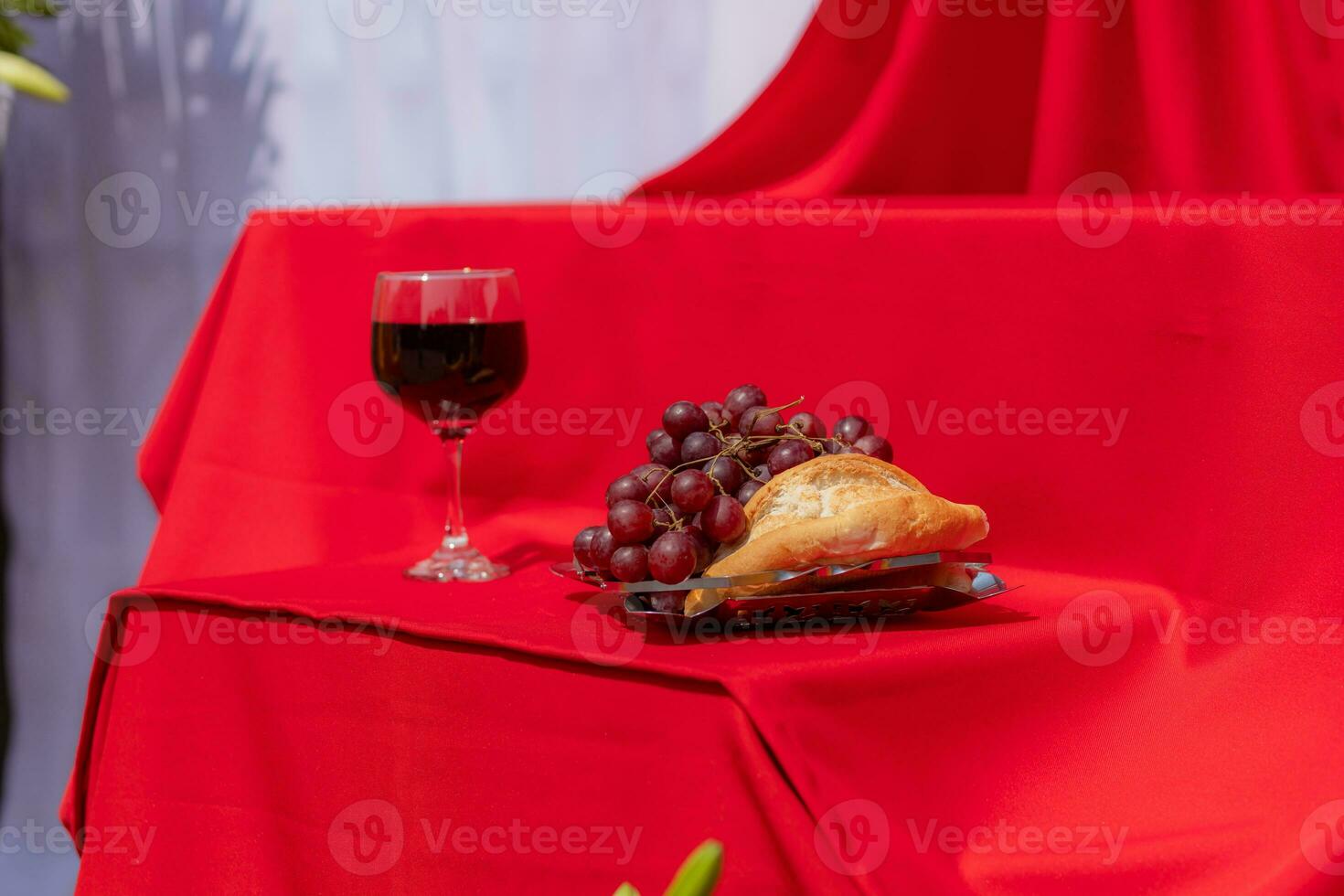 Elements of the last supper of Jesus bread, grapes and wine on a red cloth with harsh lighting photo