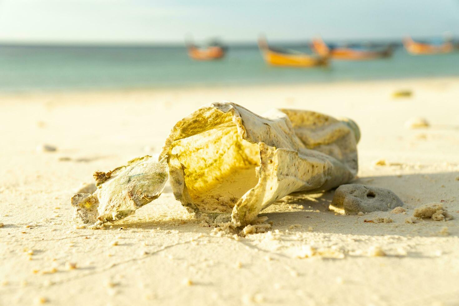 Out of focus plastic on the sand That take many years to decompose Show the problem of pollution to the environment and marine animals.Traditional fishing boats backgeound. photo