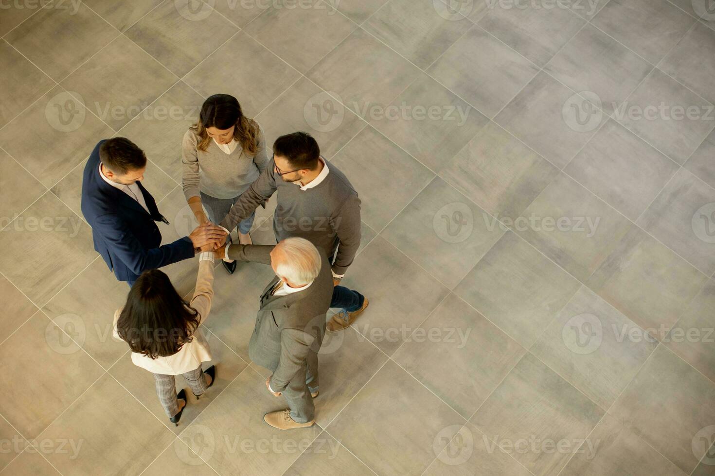 Group of young and senior business people come together in an office hallway, standing in a circle with their hands joined photo