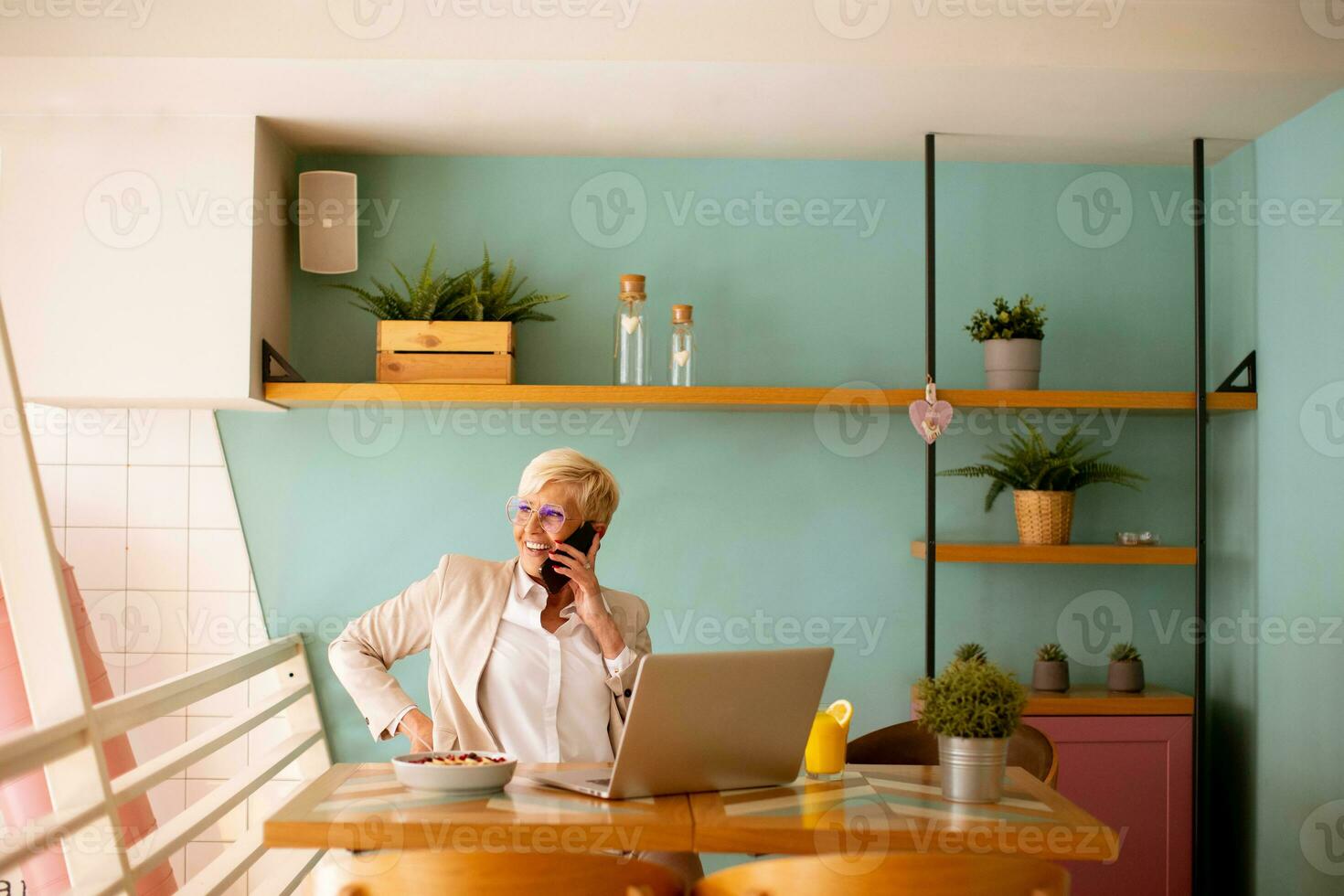 Senior woman using mobile phone while working on laptop and having healthy breakfast in the cafe photo