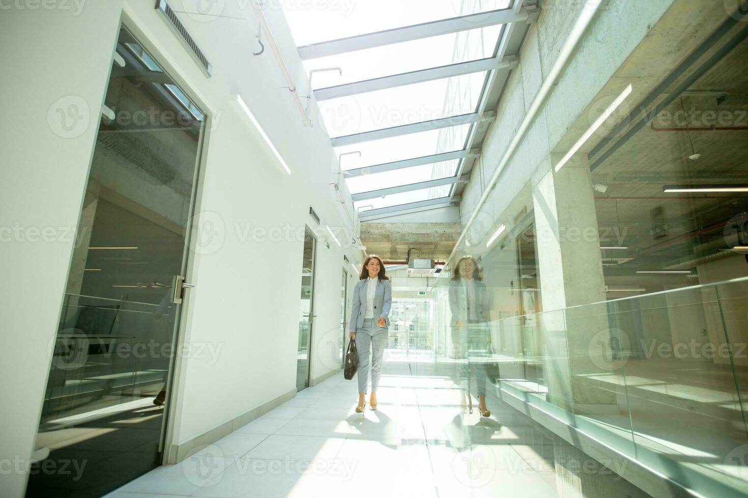 Pretty young business woman walking with briefcase in the office hallway photo