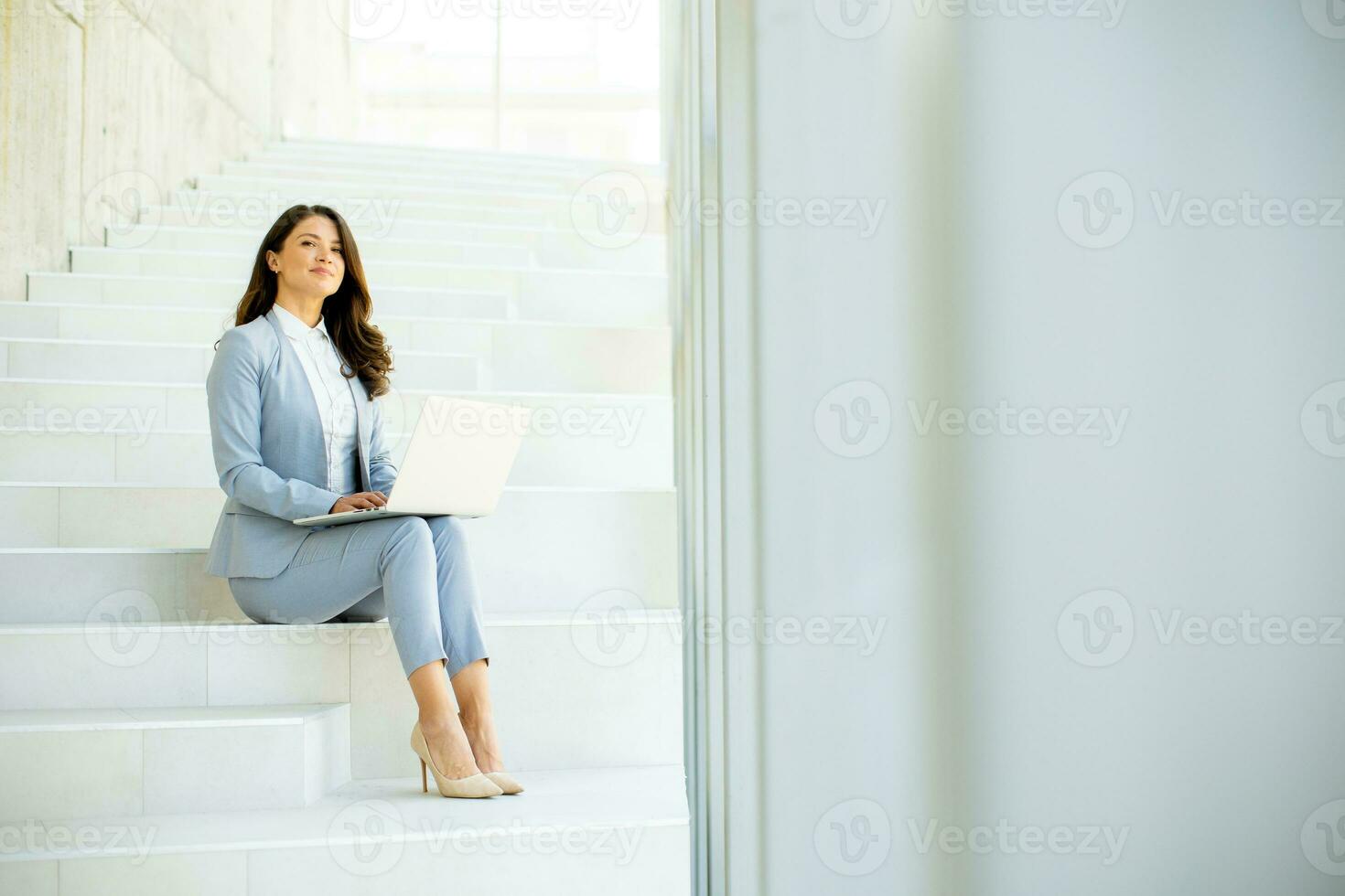Young business woman sitting on the stairs on office hallway and working on laptop photo