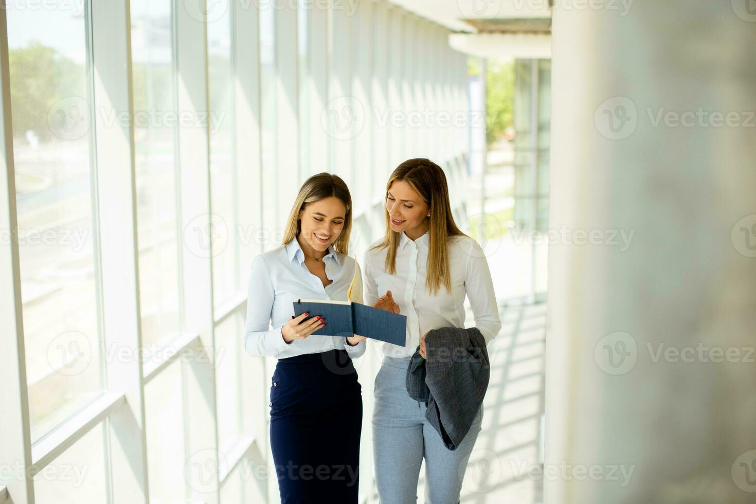 Two young business women walking on stairs in the office hallway photo