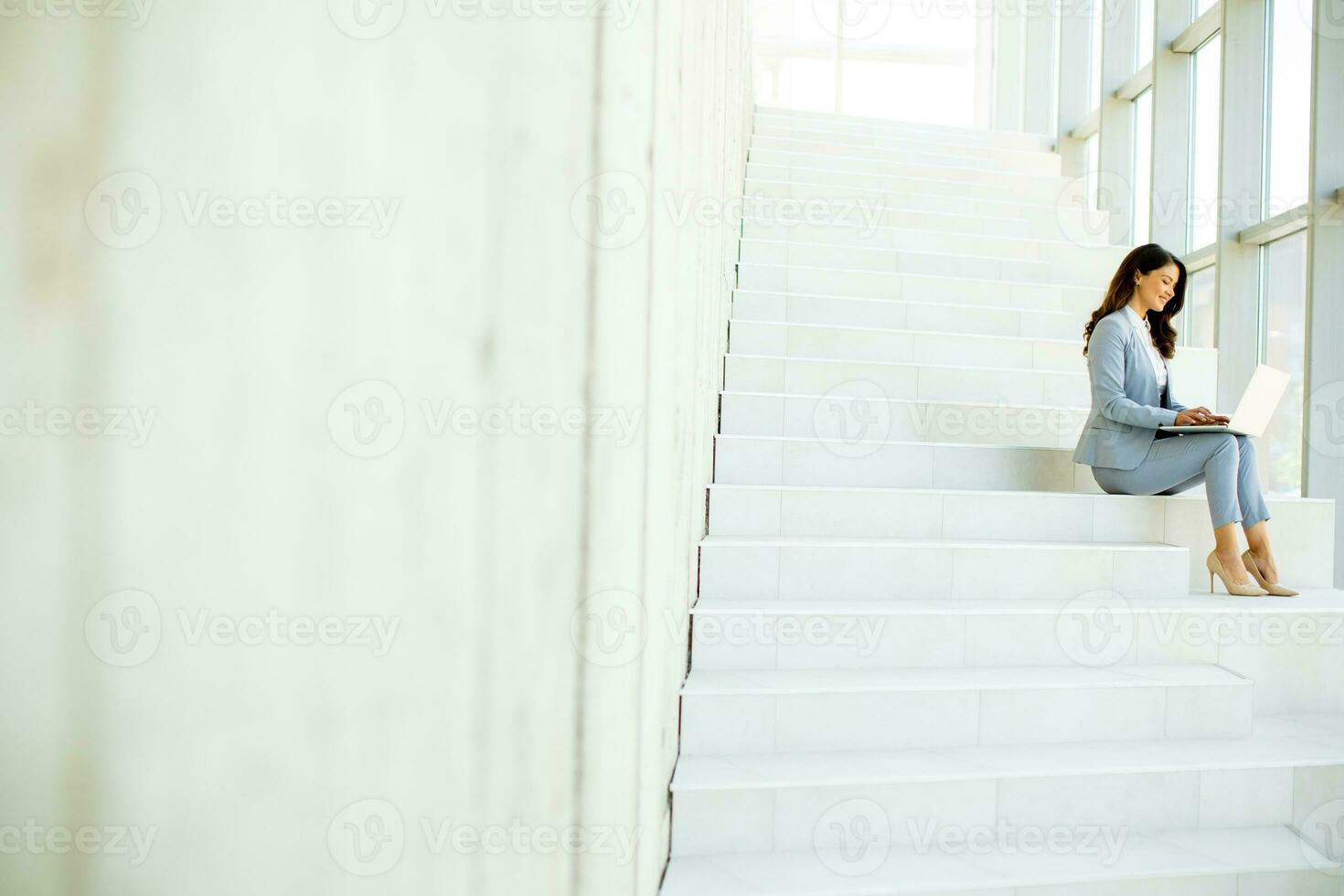 Young business woman sitting on the stairs on office hallway and working on laptop photo