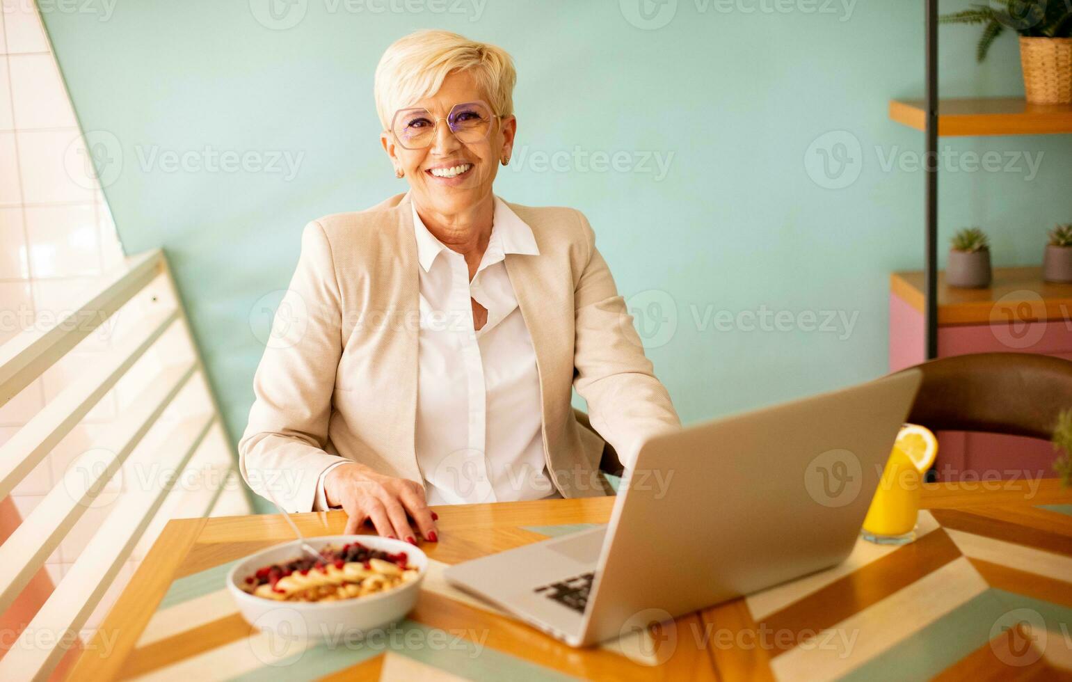 Senior woman using mobile phone while working on laptop and having healthy breakfast in the cafe photo