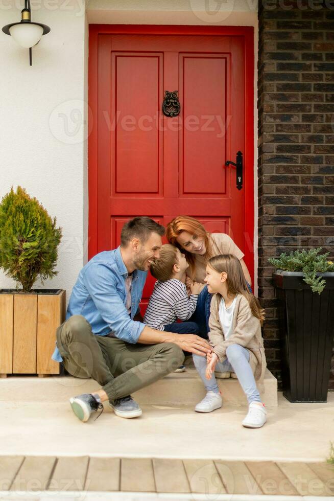 Family with a mother, father, son and daughter sitting outside on the steps of a front porch of a brick house photo