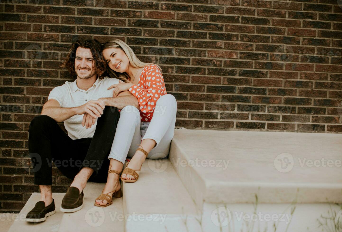 Smiling young couple in love sitting in front of house brick wall photo