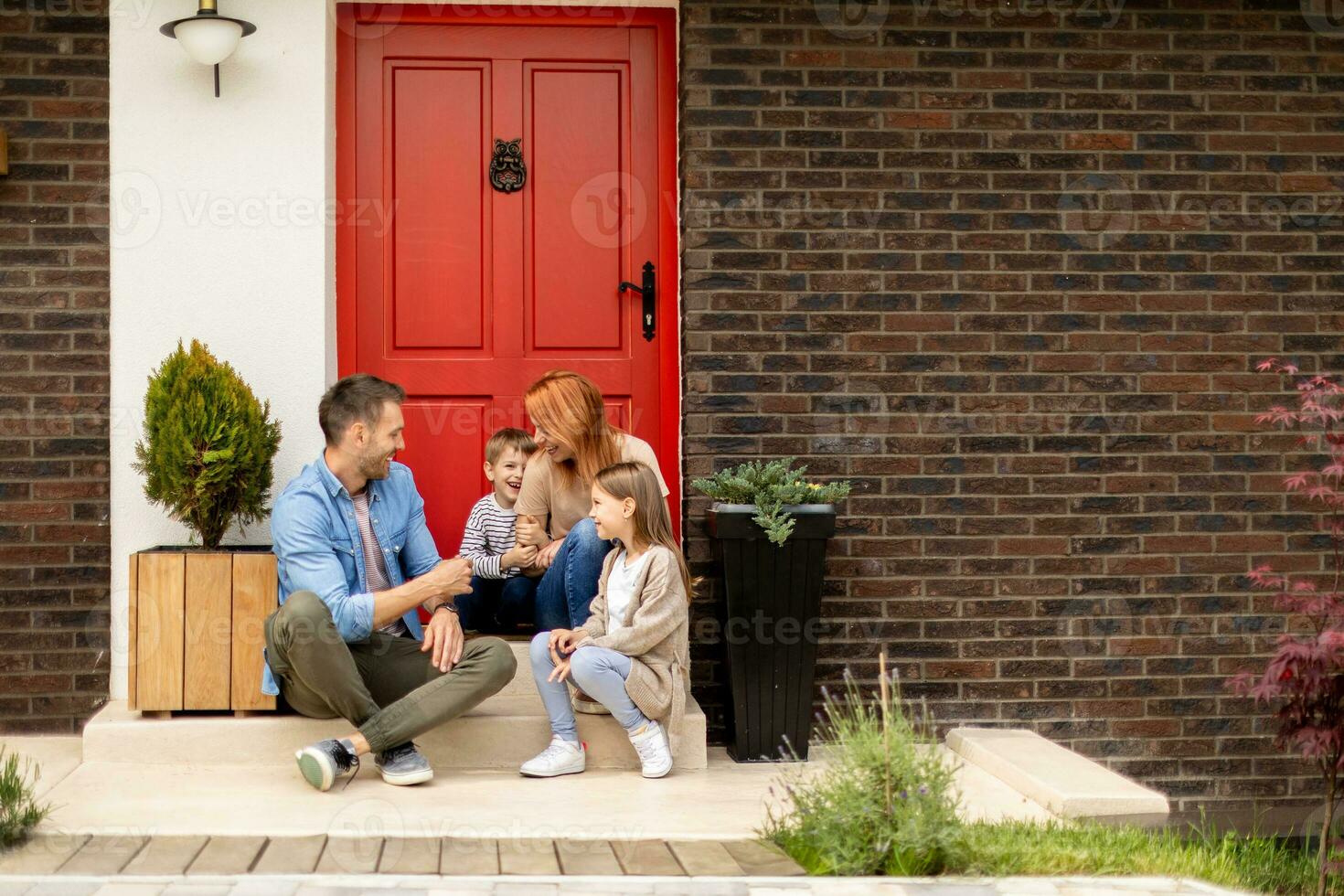 Family with a mother, father, son and daughter sitting outside on the steps of a front porch of a brick house photo